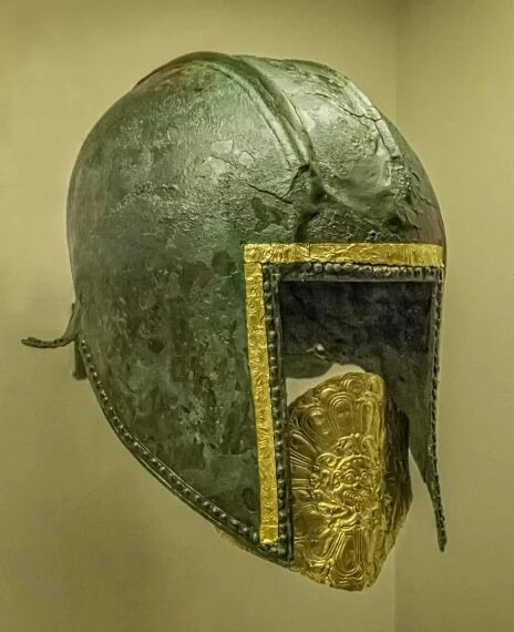  Funerary bronze helmet with gold mouth piece from the necropolis at Archontiko Greek mid-6th century BCE. This helmet features three narrow gold bands with embossed plant motifs. A multi-petalled rosette surrounding the hideous face of a Gorgon (a m