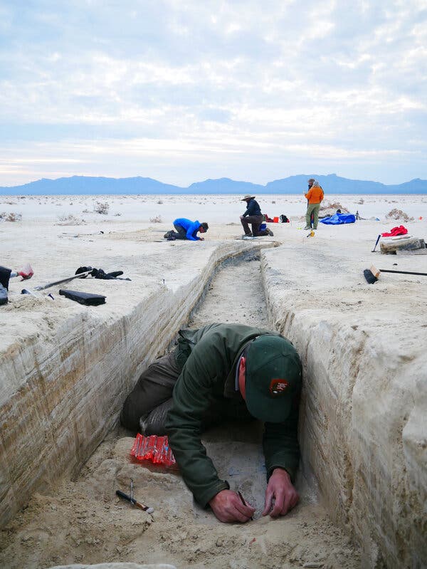 Researchers work on excavating a footprint in the bottom of a trench.
